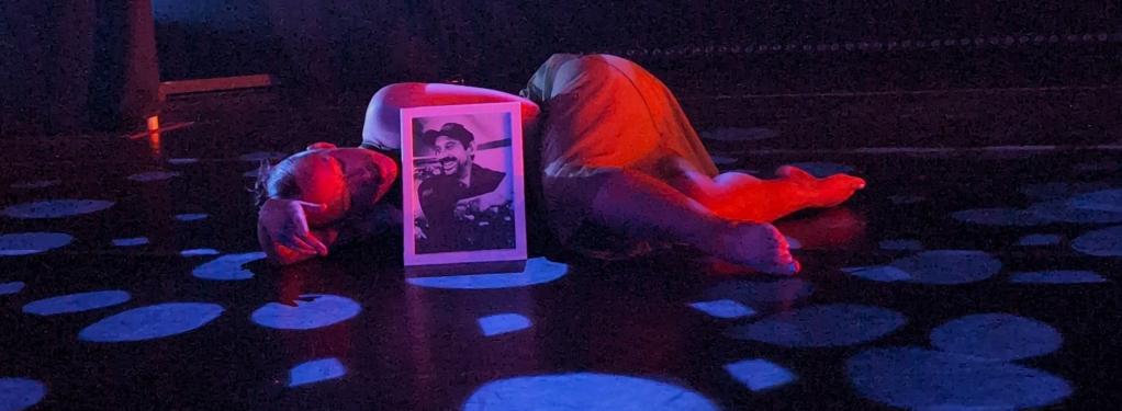 Dancer laying behind a photo frame on the floor with her silhoette lit.